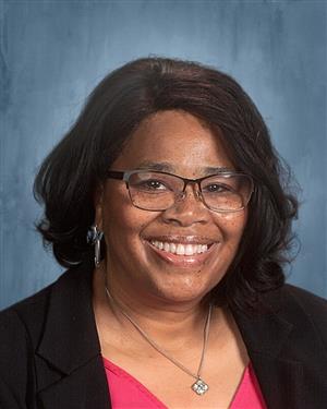 Dr. Ellerbe is wearing black glasses, a silver necklace, a pink top, and black blazer.
